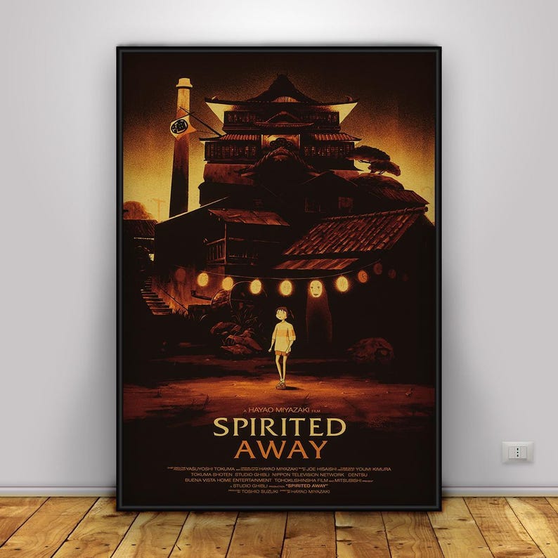 Op de afbeelding: Een ingelijste poster met de animatiefilm "Spirited Away". De afbeelding toont een jong meisje op een pad, met een traditioneel Japans gebouw op de achtergrond. De poster heeft een donker, warm kleurenpalet met de titel van de film.