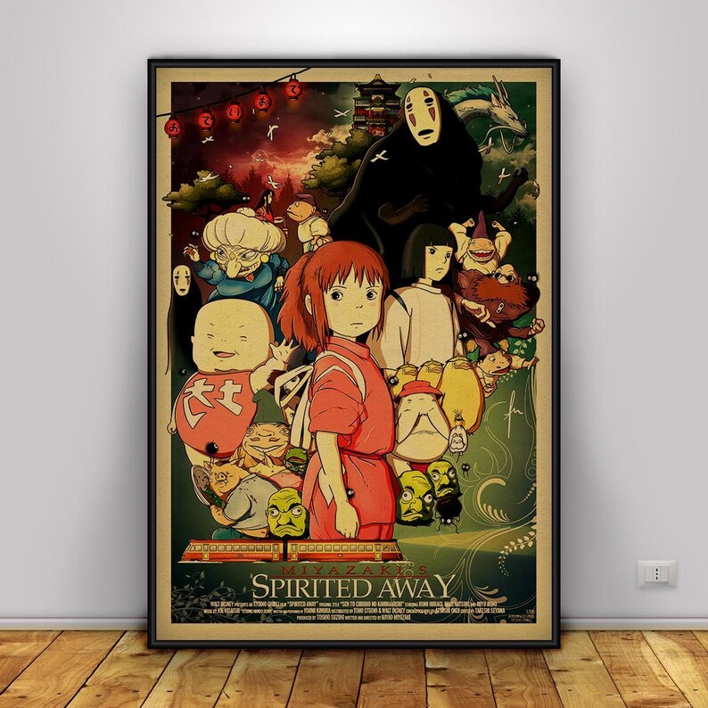 Op de afbeelding: Een ingelijste poster met personages uit de animatiefilm "Spirited Away". De afbeelding toont een meisje in een rode outfit, omringd door verschillende fantasiefiguren en de titel van de film. De poster heeft een vintage uitstraling.