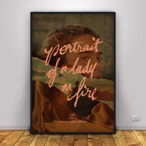 May include: A framed movie poster for "Portrait of a Lady on Fire." The poster features a portrait of a woman with the title in pink script. The background shows a landscape with a torn paper effect. The poster is in a black frame.