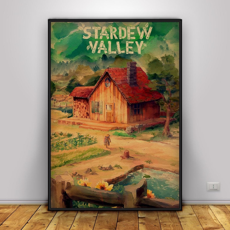 May include: A framed print featuring a watercolor painting of a cabin with a red roof and chimney, set in a valley. The text "Stardew Valley" is at the top. The scene includes a pond, fence, and fields.