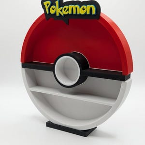 May include: A red, black, and white Pokemon-themed shelf shaped like a Poke Ball. The top features the word "Pokemon" in yellow and blue lettering. The shelf has two levels and a circular design, perfect for displaying collectibles.
