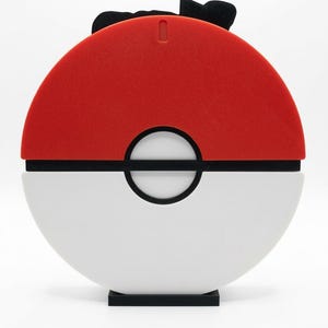 May include: A red and white sphere-shaped object with a black band and a black base. The top half is red, and the bottom half is white. A black bow-like shape is on top.