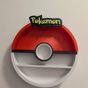 May include: A red, black, and white Pokemon-themed shelf with two levels. The top of the shelf has the word "Pokemon" in yellow and black. The shelf is round with a black circle in the middle.