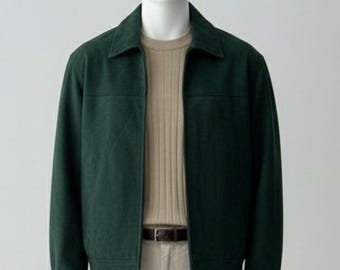 May include: A dark green zip-up jacket with a classic collar, worn over a beige ribbed jumper and light-coloured trousers with a brown belt. The jacket features a clean, structured design with long sleeves and a straight hemline, presented on a mannequin.