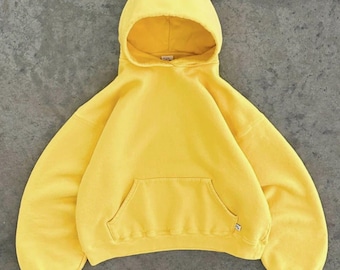 May include: A bright yellow hooded sweatshirt featuring long sleeves, a spacious hood, and a large front kangaroo pocket. The garment has a relaxed fit with ribbed cuffs and a ribbed hem, showcasing a solid, vibrant yellow colour throughout.