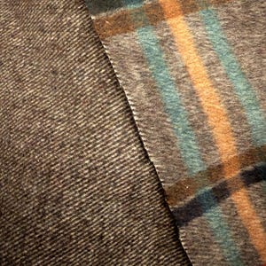 May include: A textile fabric featuring two distinct patterns. One section displays a dark brown and gray herringbone weave, while the adjacent section showcases a plaid pattern with intersecting lines in red, teal, and yellow on a gray base.