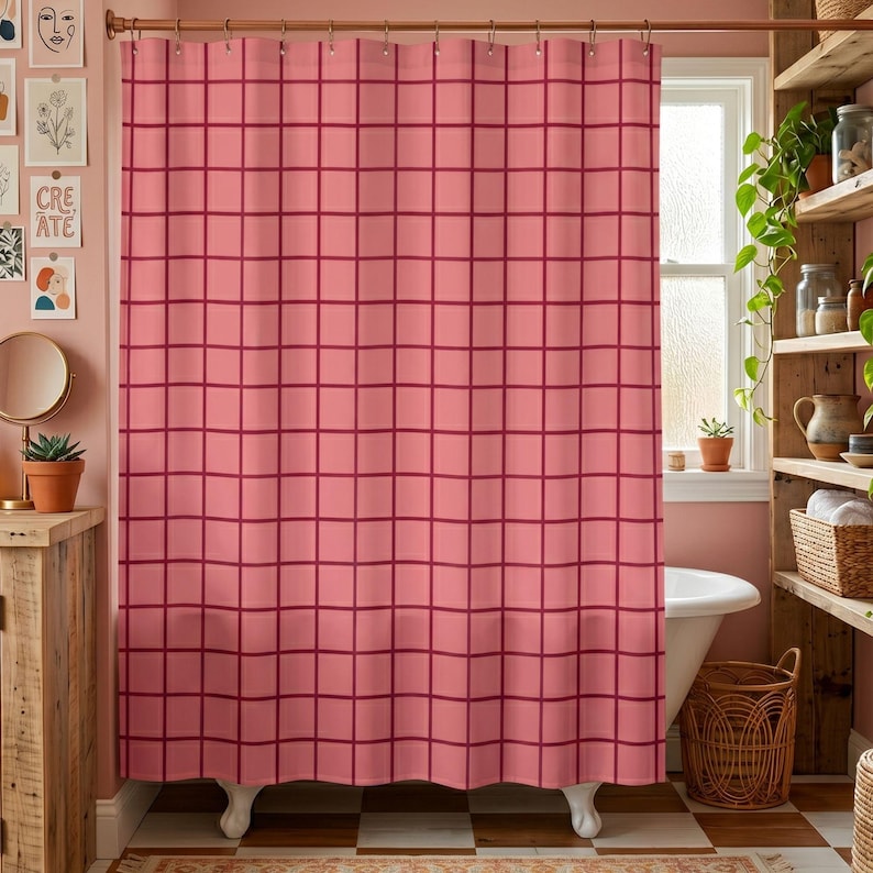 May include: A shower curtain featuring a grid pattern with dark red lines on a light pink background. The curtain hangs from a copper-colored rod with rings and covers the length of a white bathtub in a bathroom setting with tiled flooring.