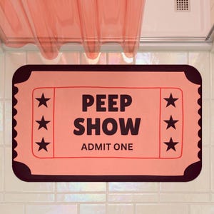 May include: A rectangular bath mat designed to look like a vintage ticket in shades of peach and dark brown. The text PEEP SHOW ADMIT ONE is printed in the centre in dark brown letters, flanked by three dark brown stars on each side.