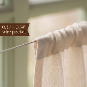 May include: A cream-colored fabric curtain featuring a top rod pocket sleeve threaded onto a thin metal wire. A brown graphic overlay indicates a 0.31 inch to 0.39 inch wire pocket size for the curtain header, showing the fabric gathered.