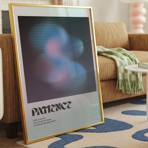 May include: A framed art print with a gold-colored frame. The artwork features a blurred, abstract design in shades of blue, pink, and black. The word "PATIENCE" is printed in a stylized font at the bottom, with additional text below.