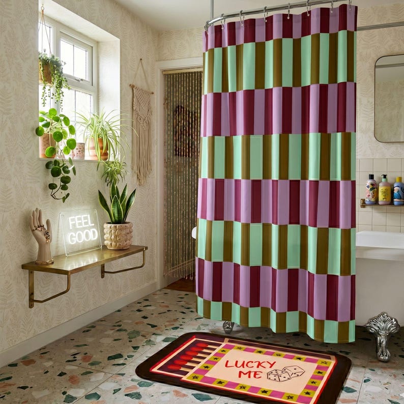 Pu&ograve; includere: Una tenda da doccia con un motivo a blocchi verticali ripetuti nelle tonalit&agrave; bordeaux, verde chiaro e lavanda. La tenda &egrave; appesa a un'asta di metallo ed &egrave; posizionata accanto a una parete del bagno con una mensola, un neon e un tappetino.