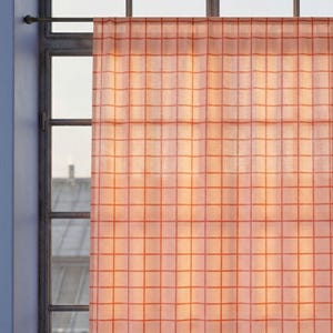 May include: A sheer, light orange curtain with a grid pattern hangs in front of a window. The curtain is made of a thin, translucent fabric, allowing light to filter through. The grid pattern is created by thin, orange lines.