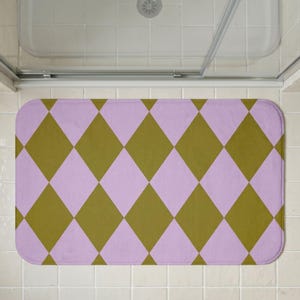 May include: A rectangular bath mat featuring a repeating harlequin diamond pattern in alternating shades of muted olive green and soft pastel lavender. The mat has rounded corners and a flat, uniform texture across the entire surface area.