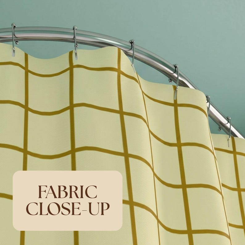 Pu&ograve; includere: Una tenda da doccia con un motivo a griglia a linee giallo senape su sfondo color crema pallido, appesa a un'asta curva in metallo argentato con anelli. Un'etichetta beige riporta il testo FABRIC CLOSE-UP.