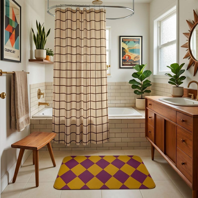 May include: A rectangular bath mat featuring a repeating diamond pattern in alternating shades of mustard yellow and deep purple. The mat has rounded corners and lies flat on a tiled floor in front of a wooden vanity and a bathtub with a grid curtain.