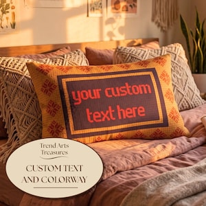 May include: A rectangular throw pillow featuring an orange background with a repeating red snowflake pattern. A dark purple rectangular border frames the center, which displays the red text "your custom text here" in a bold, blocky font.