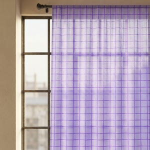 May include: A sheer purple curtain with a grid pattern hangs in front of a window. The curtain is made of a lightweight fabric and allows light to filter through. The window has a dark metal frame.