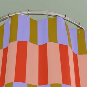Pu&ograve; includere: Una tenda da doccia appesa a un'asta metallica curva con anelli argentati. Il tessuto presenta un motivo a righe verticali ripetute con bande alternate nei colori viola chiaro, giallo senape, arancione brillante e pesca tenue.