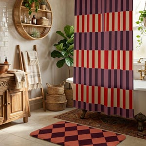 May include: A shower curtain featuring a repeating vertical striped pattern in shades of deep purple, bright red, and cream. The fabric hangs in front of a bathtub, coordinating with a rectangular bath mat displaying a purple and red diamond pattern.