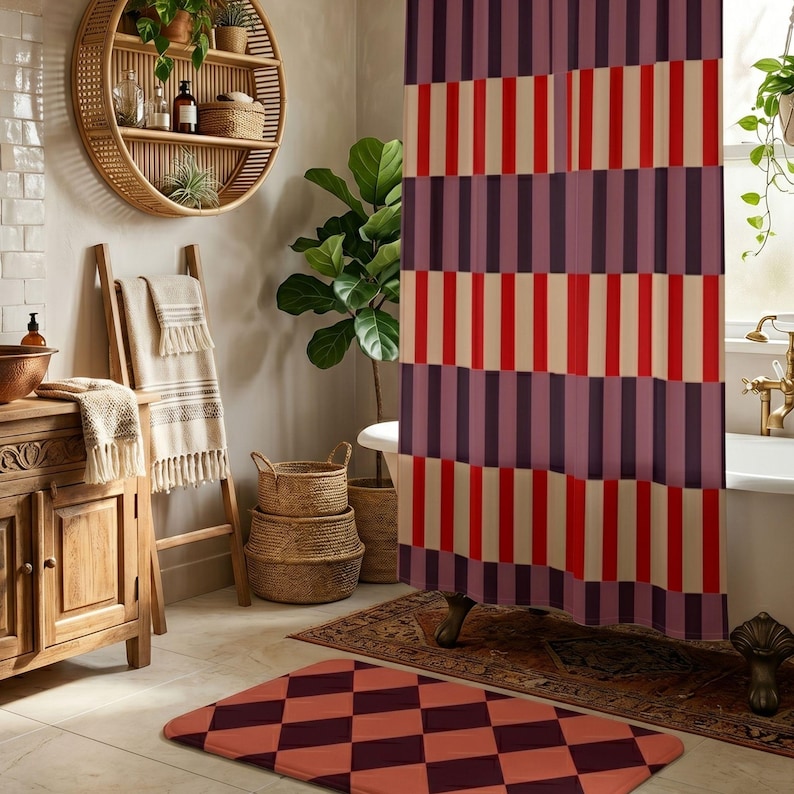 May include: A shower curtain featuring a repeating vertical striped pattern in shades of deep purple, bright red, and cream. The fabric hangs in front of a bathtub, coordinating with a rectangular bath mat displaying a purple and red diamond pattern.