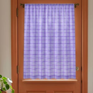 May include: A light purple curtain featuring a darker purple grid pattern. The curtain is hung on a horizontal rod and displays a semi-sheer fabric texture with vertical folds, covering the center portion of a solid orange door frame.