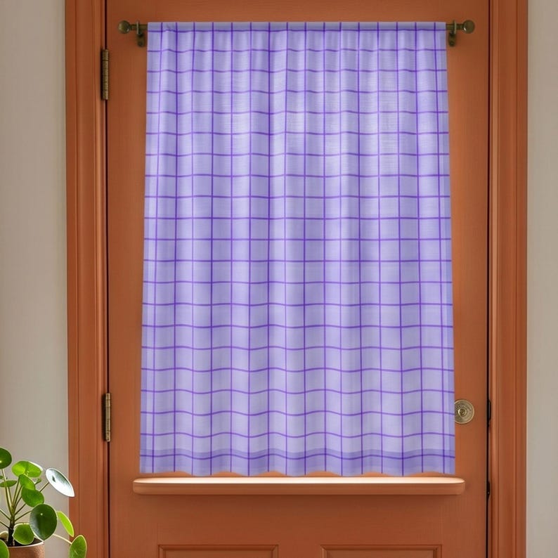May include: A light purple curtain featuring a darker purple grid pattern. The curtain is hung on a horizontal rod and displays a semi-sheer fabric texture with vertical folds, covering the center portion of a solid orange door frame.