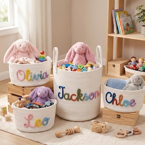 Puede incluir: Cuatro cestas de almacenamiento de cuerda blanca con nombres bordados de colores: Olivia, Jackson, Leo y Chloe. Cada cesta contiene juguetes, incluyendo conejos de peluche, bloques de madera y coches de juguete. Las cestas están sobre una alfombra clara.