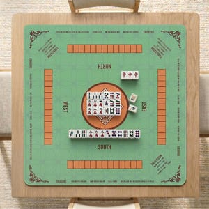 Puede incluir: Un tablero de juego de Mahjong verde con ranuras para fichas naranjas y diseños decorativos en las esquinas. El tablero presenta fichas dispuestas en un patrón circular, con las palabras "Norte", "Este", "Oeste" y "Sur" visibles.