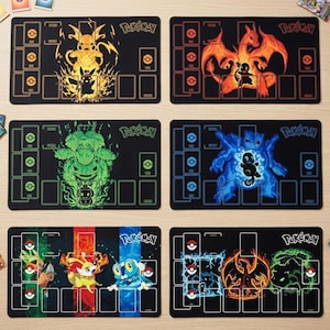 Può includere: Sei tappetini da gioco rettangolari neri per giochi di carte collezionabili, ognuno con grafiche Pokémon e layout di gioco. I design includono Pikachu, Charizard, Venusaur, Blastoise e vari Pokémon iniziali, con il logo Pokémon.