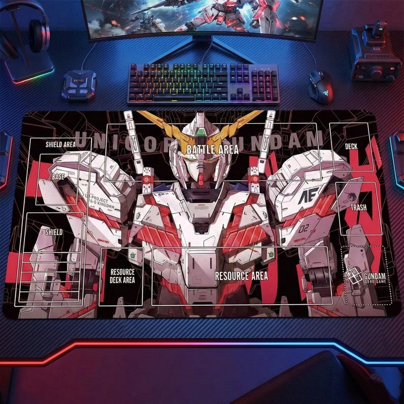 May include: Black gaming mousepad featuring a detailed illustration of a Gundam robot with red, white, and gold accents. The mat includes labeled areas for card game play, such as "Battle Area" and "Resource Area."