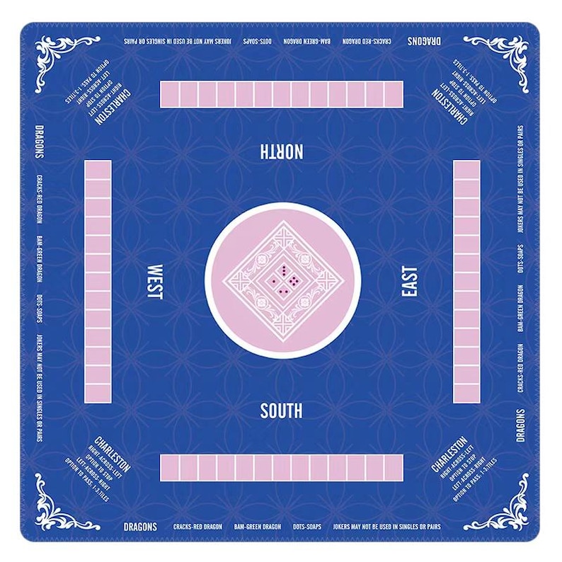 May include: A square blue Mahjong mat featuring a central white circle with a diamond pattern and dice. The mat includes labeled North, South, East, and West positions, along with Charleston instructions and rectangular tile racks in light pink.
