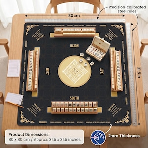 May include: A square Mahjong mat measuring 80 cm by 80 cm, approximately 31.5 inches by 31.5 inches, with a black surface, gold compass points, and four wooden tile racks. Includes a small open box of tiles, score sheets, and a pencil.