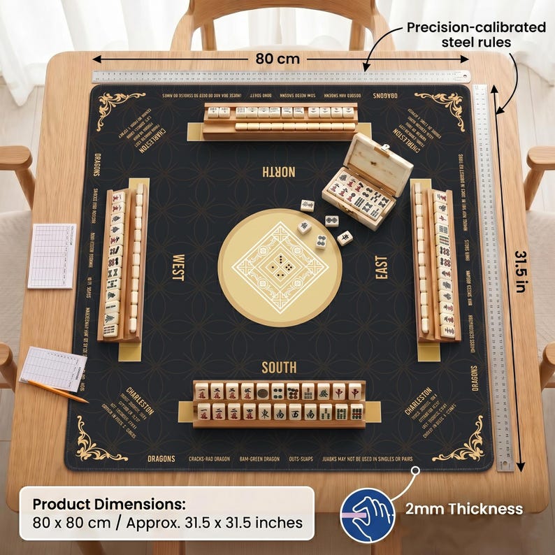May include: A square Mahjong mat measuring 80 cm by 80 cm, approximately 31.5 inches by 31.5 inches, with a black surface, gold compass points, and four wooden tile racks. Includes a small open box of tiles, score sheets, and a pencil.