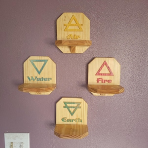 May include: Four wooden shelves, each representing an element: Air, Water, Fire, and Earth. Each shelf has a unique symbol and color, with the element's name below. The shelves are mounted on a purple wall.