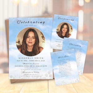 May include: A collection of memorial cards with a portrait of a woman, set against a sky-blue background with cloud imagery. The cards include the text "Celebrating the Life Of" and details such as name, dates, and service information. The cards are on a wooden surface.