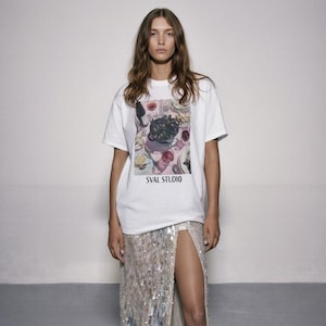 May include: A woman in a white t-shirt with a graphic and "SVAL STUDIO" text, paired with a long, sequined skirt featuring a high split and white trainers. The skirt has a gradient effect, transitioning in colour.