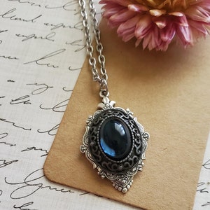 May include: A silver chain necklace with a pendant featuring a dark blue oval-shaped gemstone set in a silver filigree frame.