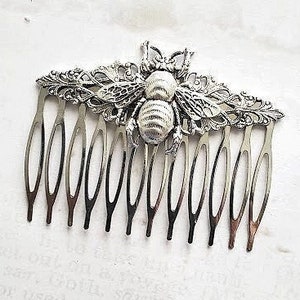 May include: Silver hair comb featuring an intricate bee design. The bee is crafted from metal and has a textured, white finish.
