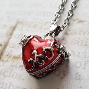 May include: A silver chain necklace with a red heart-shaped pendant. The pendant has an intricate design with silver accents.