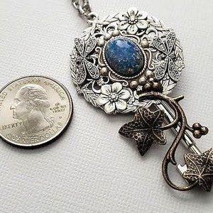 May include: A silver necklace with a key pendant featuring a blue gemstone surrounded by floral and dragonfly details. The key has a bronze ivy vine design.