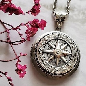 Puede incluir: Un collar con un dije de brújula de plata, con un diseño de brújula detallado y una pequeña piedra que parece un diamante en el centro. El collar tiene una cadena de plata.