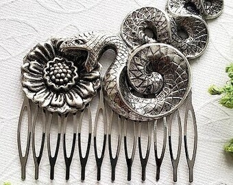 May include: Silver hair comb with a detailed snake and flower design. The snake is curled around the flower and has a textured surface.