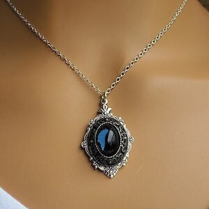 Peut inclure: Un collier en cha&icirc;ne argent avec un pendentif ovale noir orn&eacute; d'un motif de papillon bleu. Le pendentif est serti dans un cadre en filigrane argent.