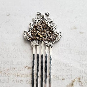 May include: A silver hair comb with a floral design. The flowers are gold and have a raised design. The comb has five tines.