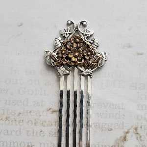 May include: A silver hair comb with a gold floral design. The comb has five tines and a decorative top.