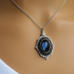 Peut inclure: Un collier en cha&icirc;ne argent avec un pendentif orn&eacute; d'une pierre ovale bleu fonc&eacute; sertie dans un cadre en filigrane argent.