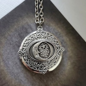 Puede incluir: Collar con dije de plata con un diseño filigranado detallado. El dije presenta una luna creciente con una estrella y una cara.