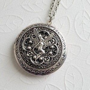 May include: Silver locket necklace with a detailed design featuring a fairy with wings. The locket has a filigree pattern and is on a silver chain.