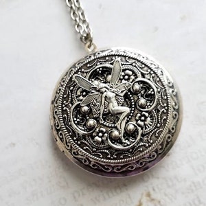 May include: Silver locket necklace with a detailed filigree design featuring a fairy with wings. The locket has a round shape and a silver chain.