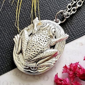 Puede incluir: Collar de plata con un dije en forma de rana detallada. El dije es de forma ovalada y tiene una cadena.